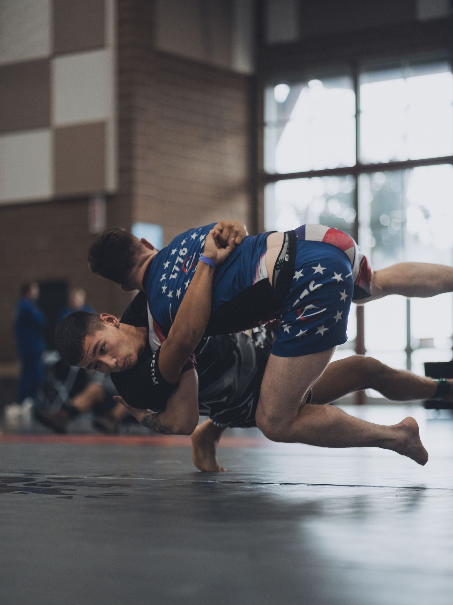 A wrestler in patriotic shorts performs a takedown move during a match.