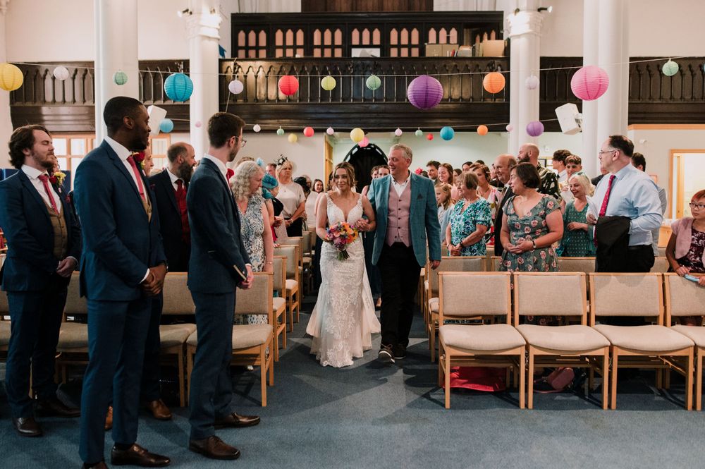 Wedding guests stand in a church decorated with colorful paper lanterns during a ceremony.