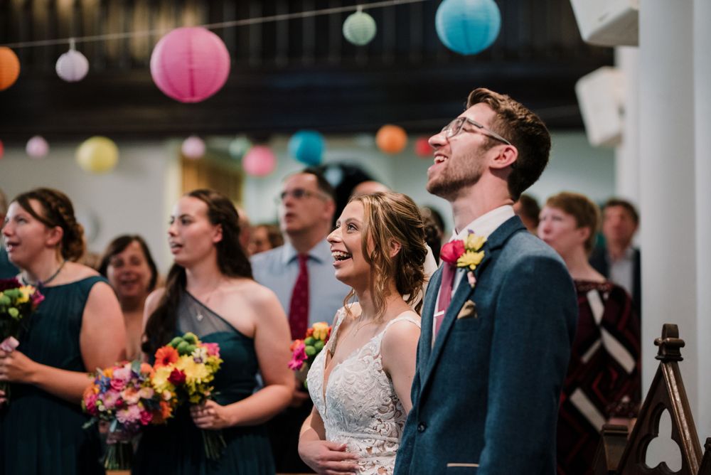 Wedding party smiling and laughing during ceremony under colorful paper lanterns.