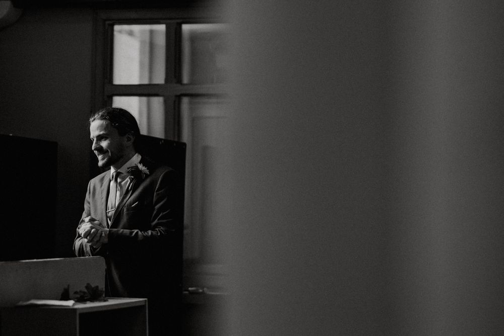 Black and white portrait of person in formal attire by a window.