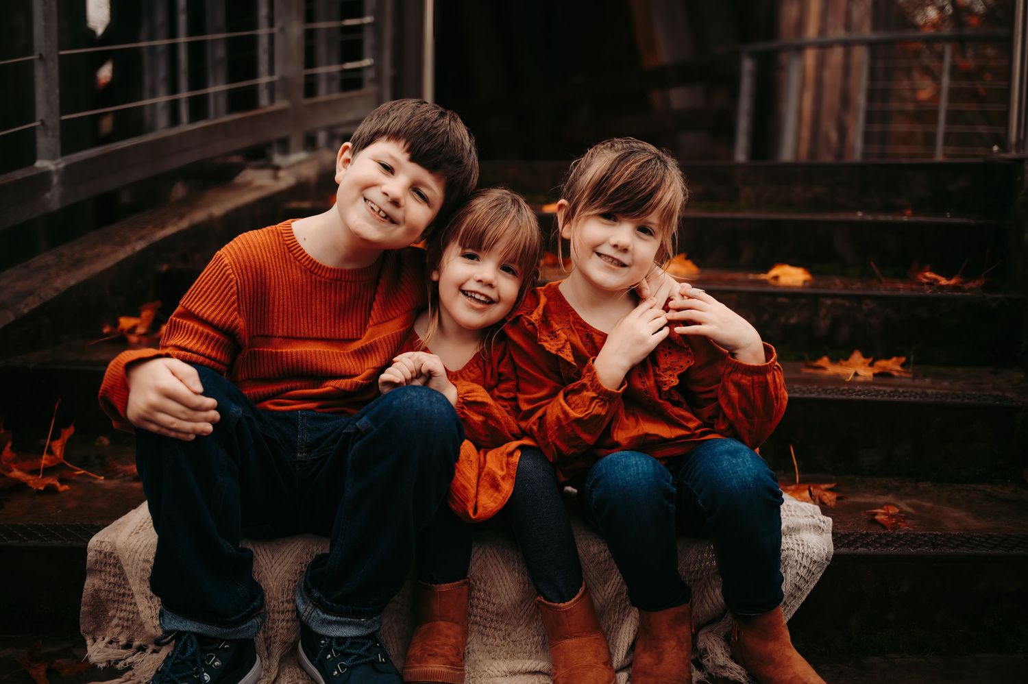 Children sitting together on wooden steps wearing orange and blue clothing.