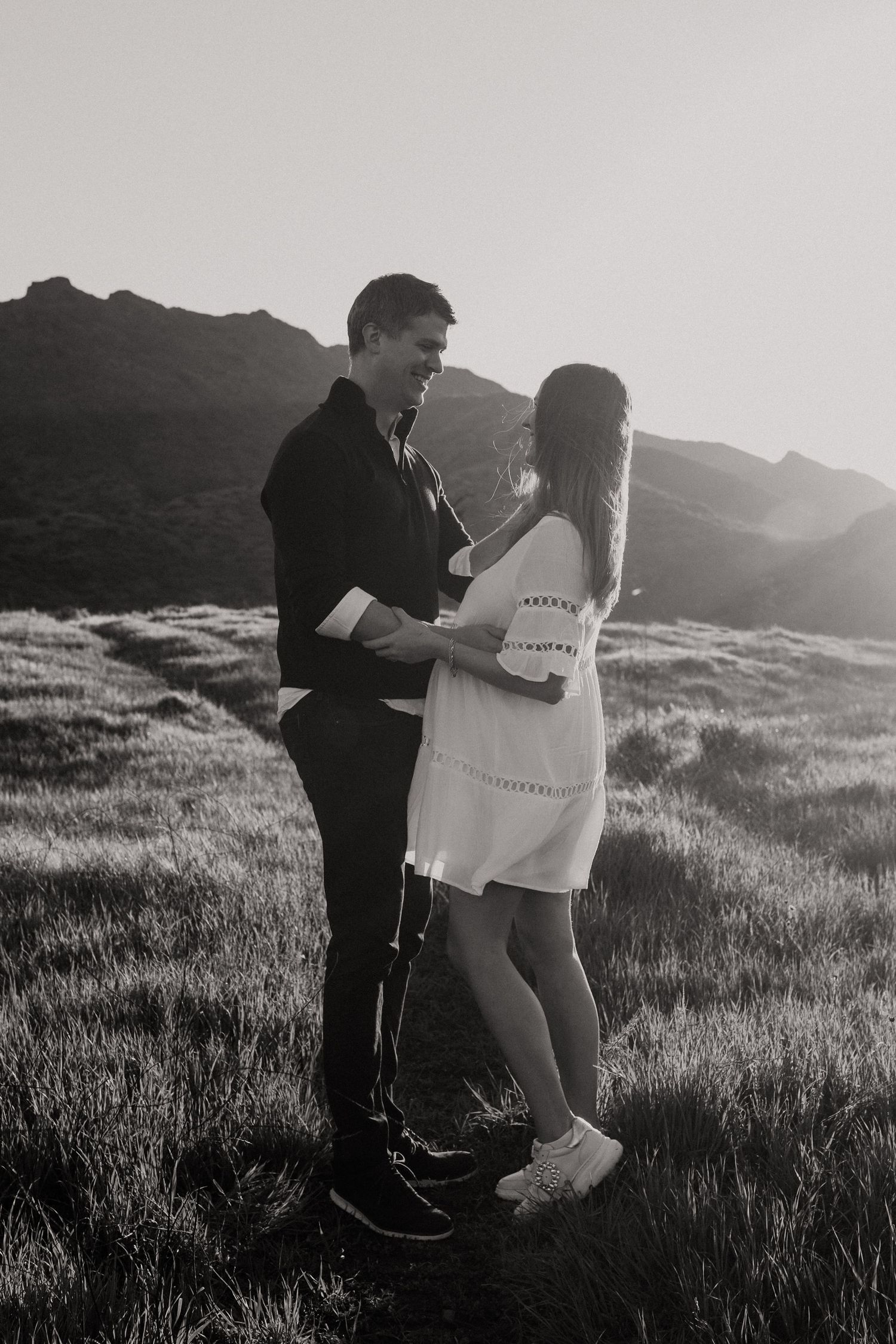 A tender black and white photo of a couple embracing on a mountainside at sunset.