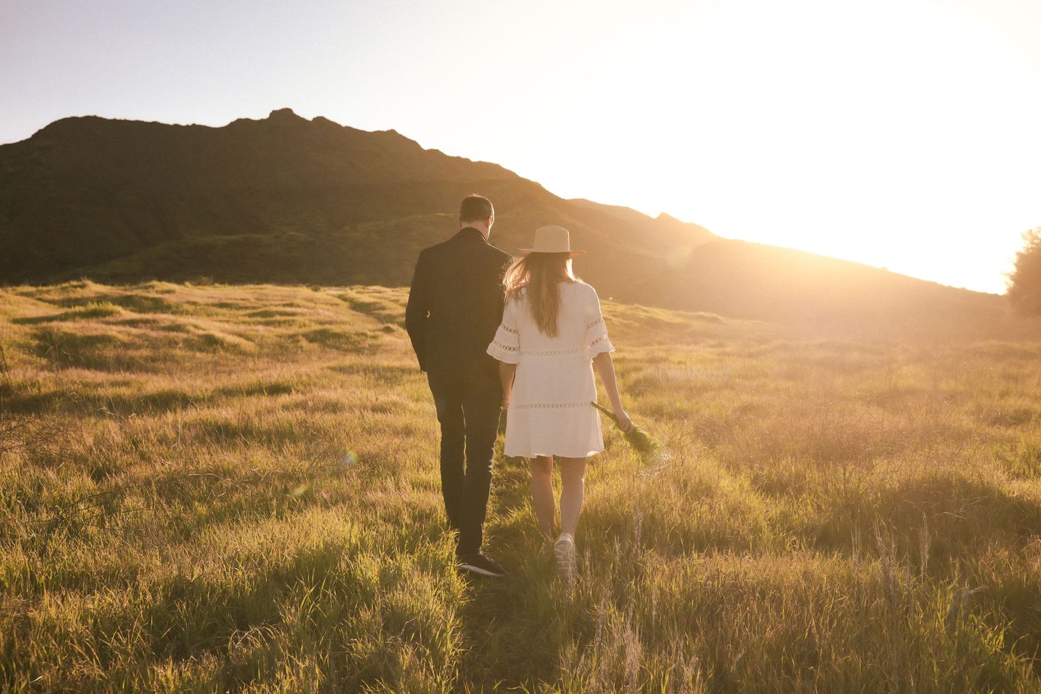 Couple walking together through mountain meadow at golden hour.