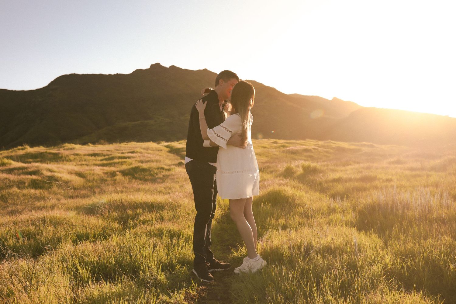 A romantic sunset portrait of two people standing together in a golden mountain meadow.