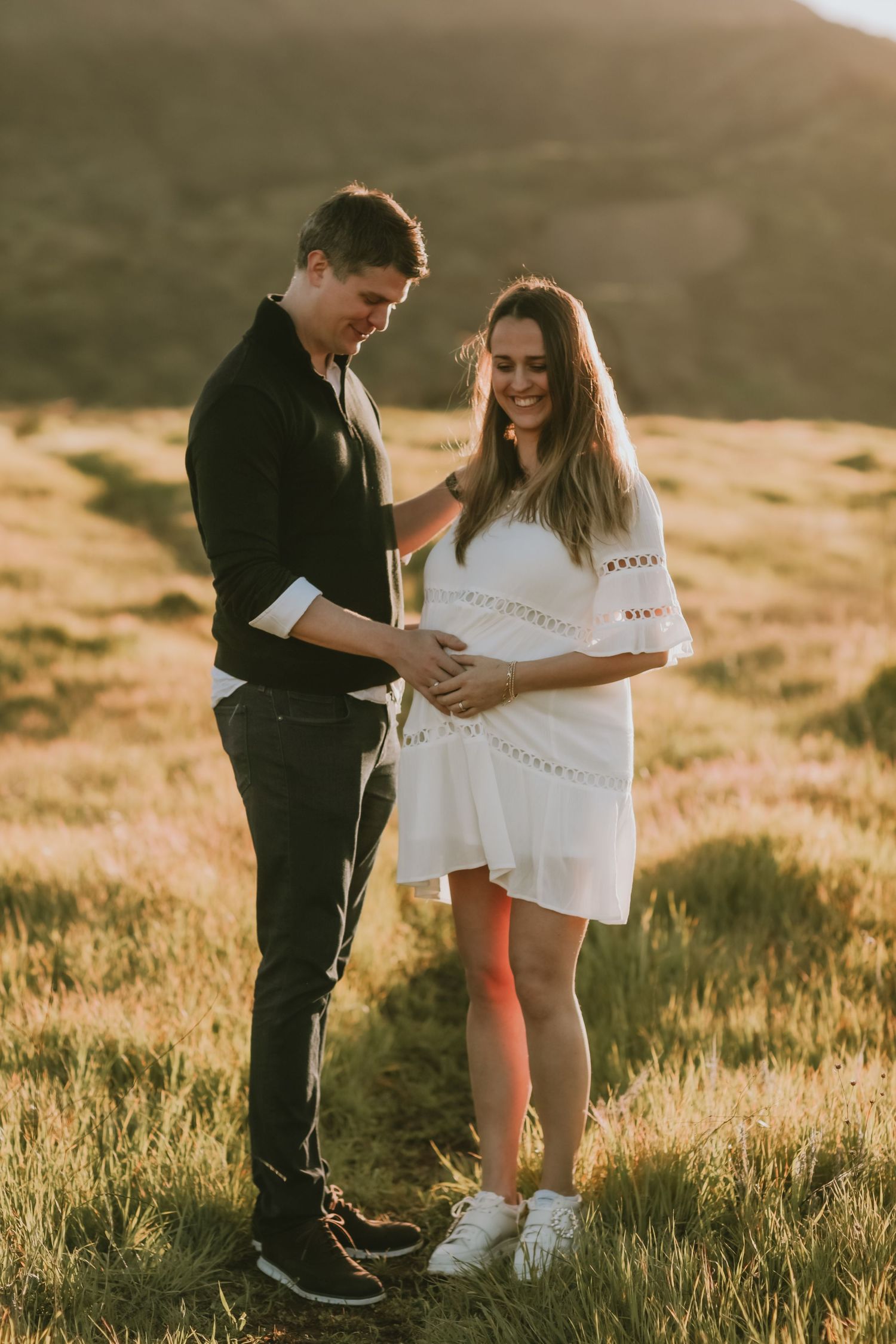 A couple shares a tender moment in golden light on a grassy mountainside.
