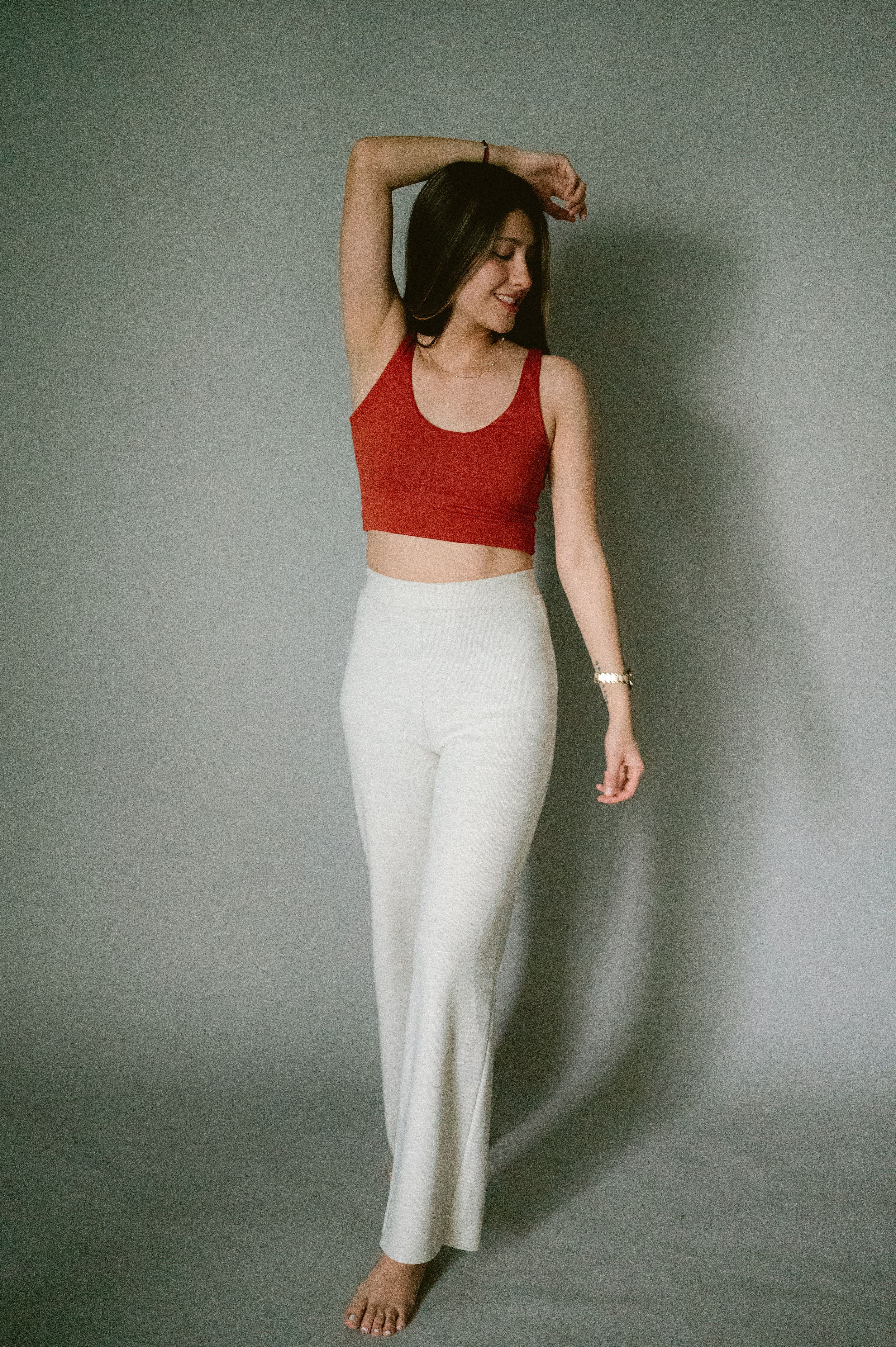 Model wearing red crop top and white pants poses elegantly against gray background.