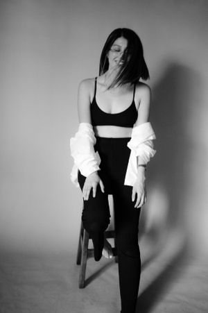 Monochrome studio portrait in athletic wear and white cardigan with dramatic shadows.