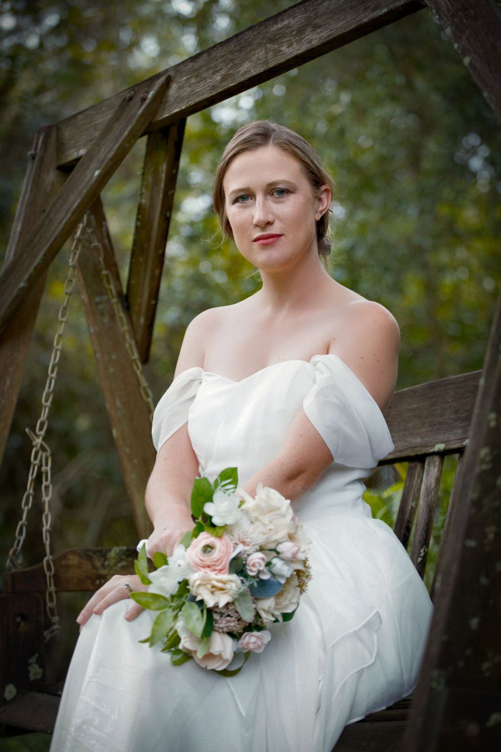 A bride sitting on a wooden bench swing.