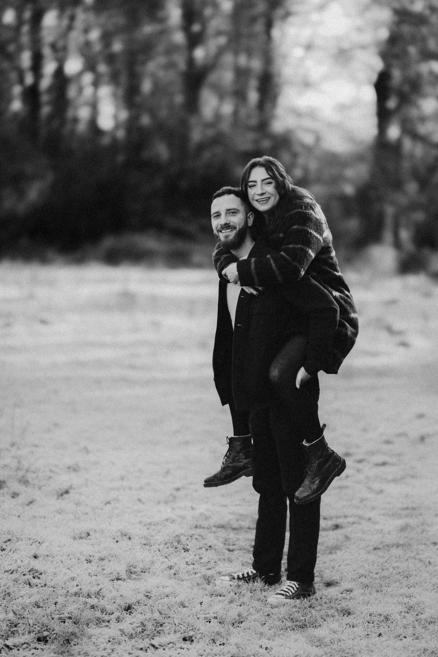 Playful couple enjoying a piggyback ride in a misty black and white forest setting.