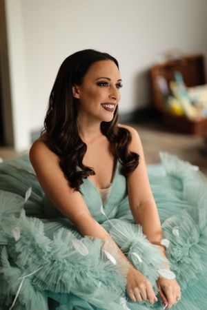 Woman in mint green tulle gown smiles elegantly in soft indoor lighting.