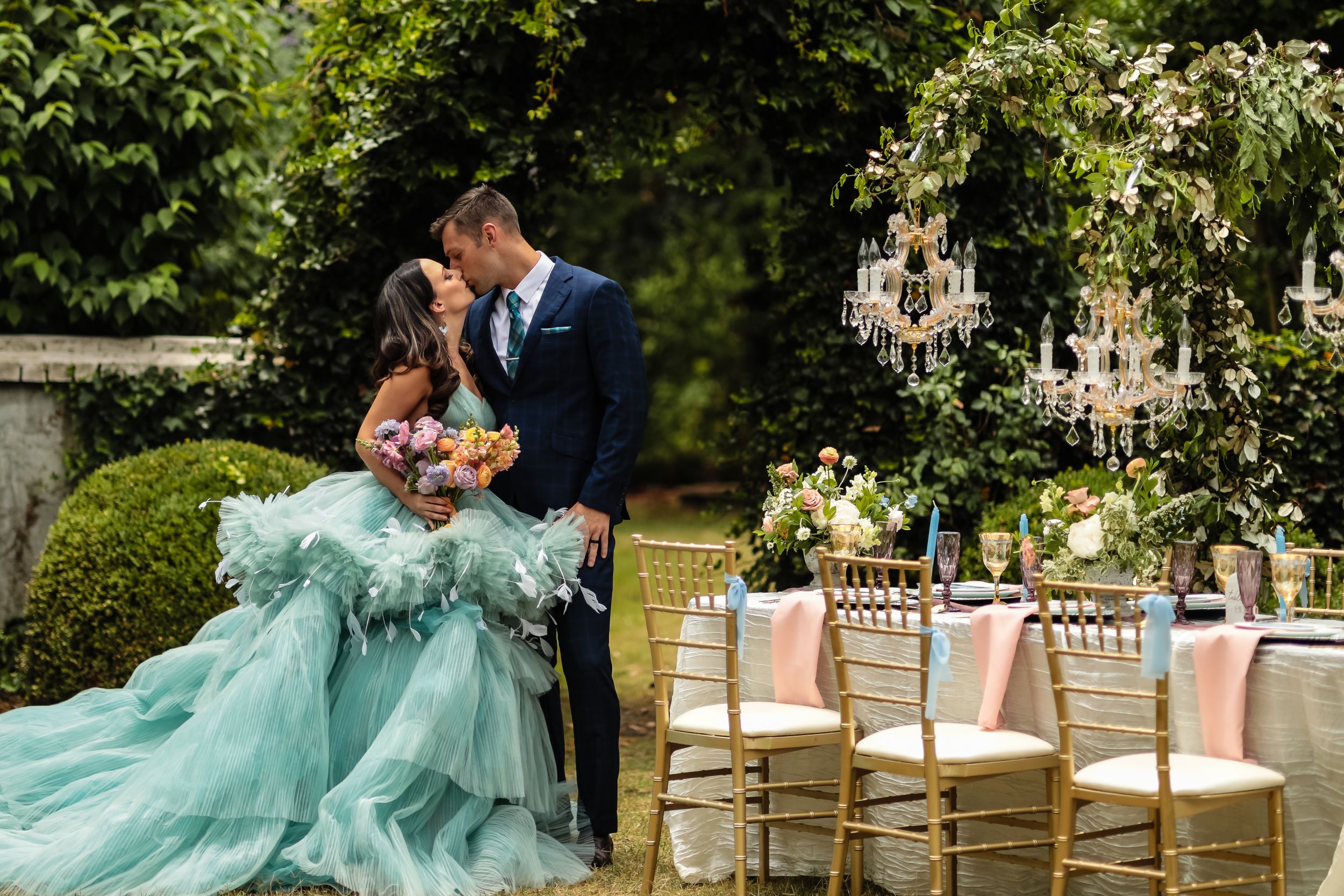 Couple shares intimate moment in garden setting with elegant outdoor reception decor.