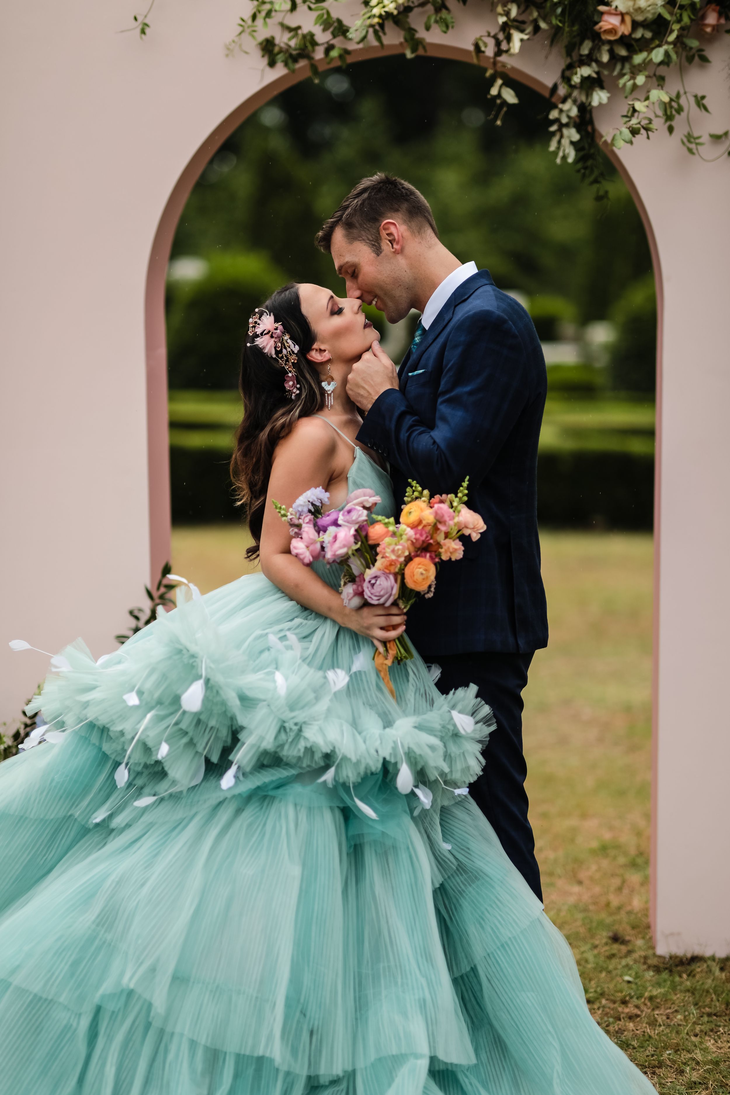 Romantic couple shares an intimate moment under an archway with the bride wearing a stunning mint green tulle gown.