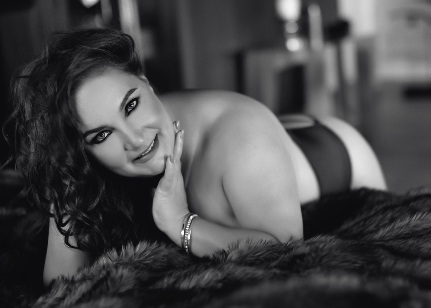 Black and white boudoir photograph showing a curled up figure reclining on dark textured bedding.