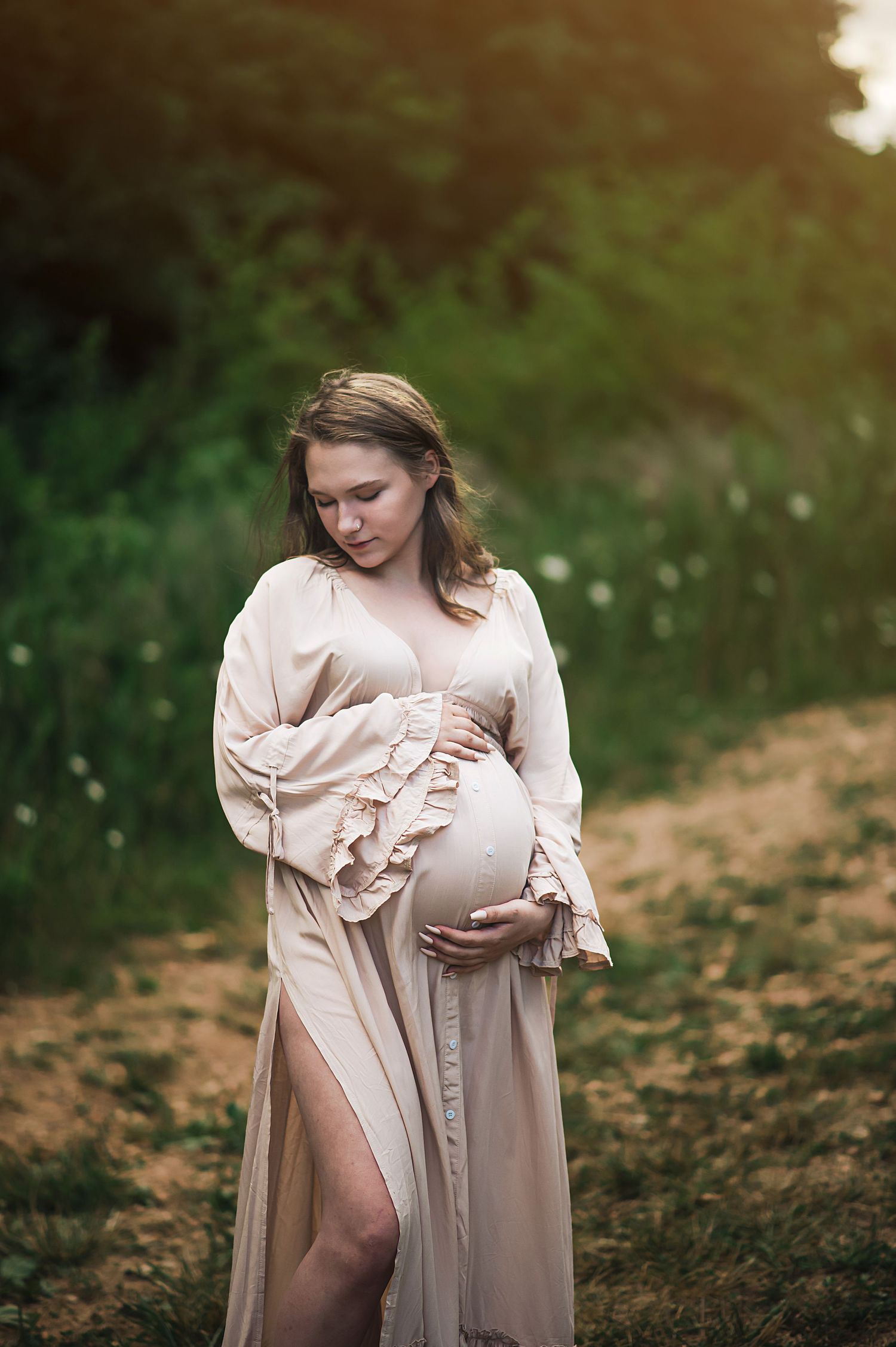 A maternity portrait in a cream-colored dress amid wildflowers at golden hour.