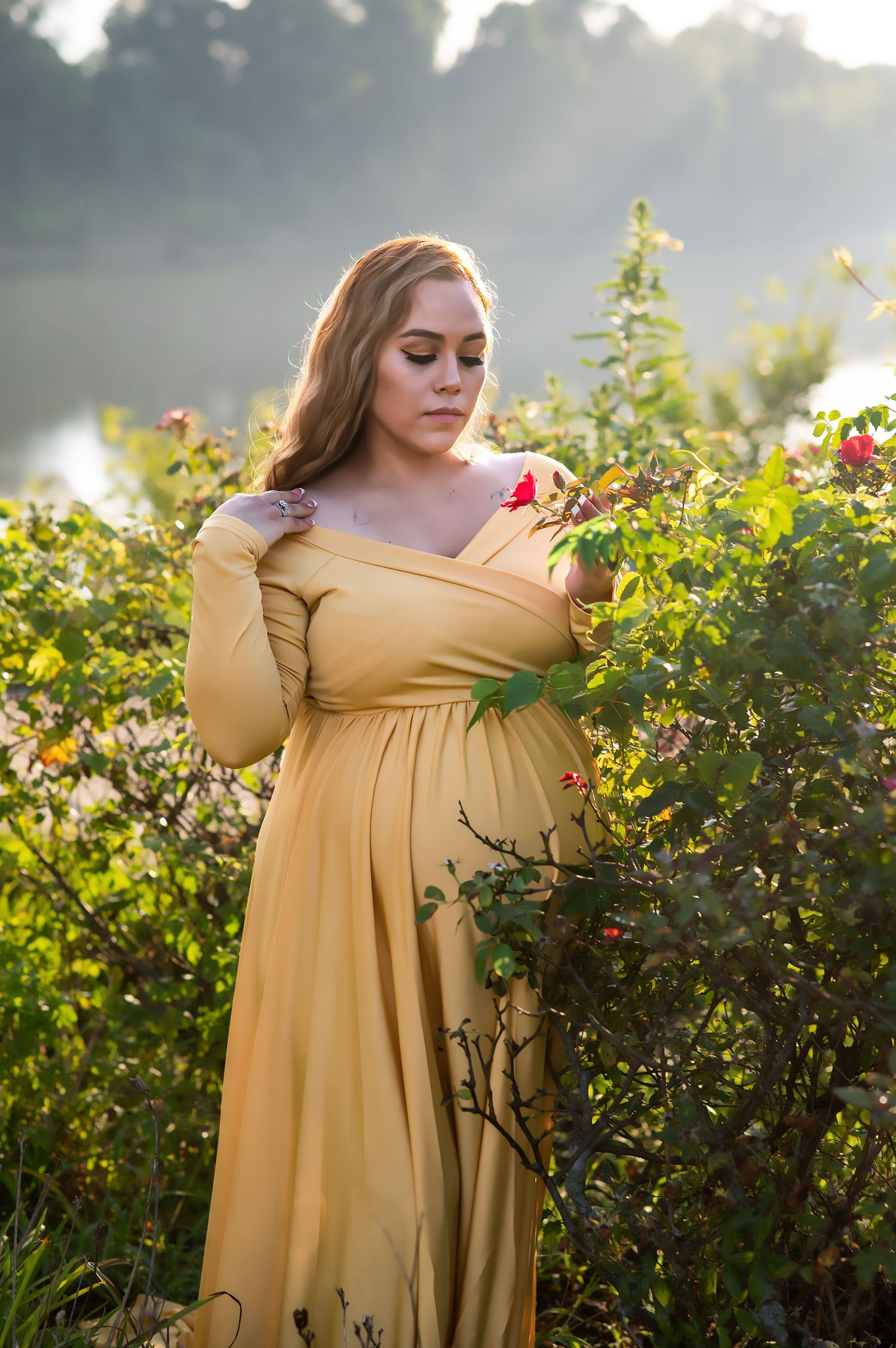 Ethereal maternity portrait in yellow dress among blooming garden at sunset.
