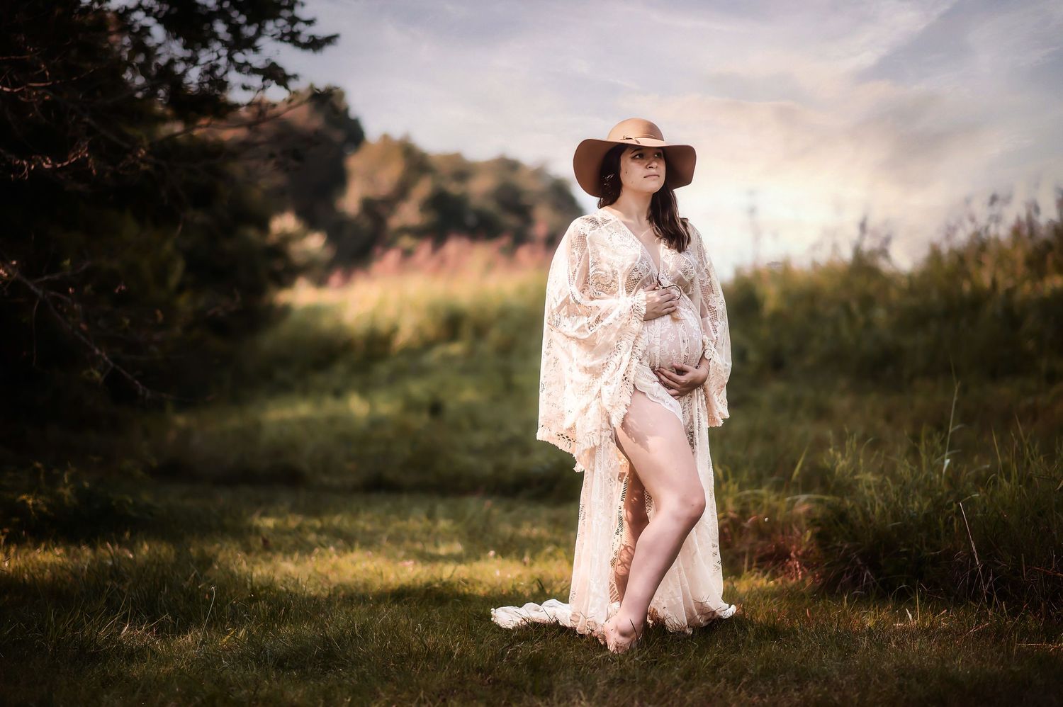 Maternity portrait in flowing dress and hat during golden sunset.