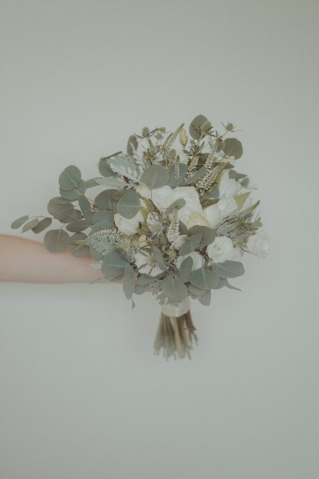 Um delicado bouquet de noiva com flores brancas e folhas de eucalipto sobre um fundo claro.