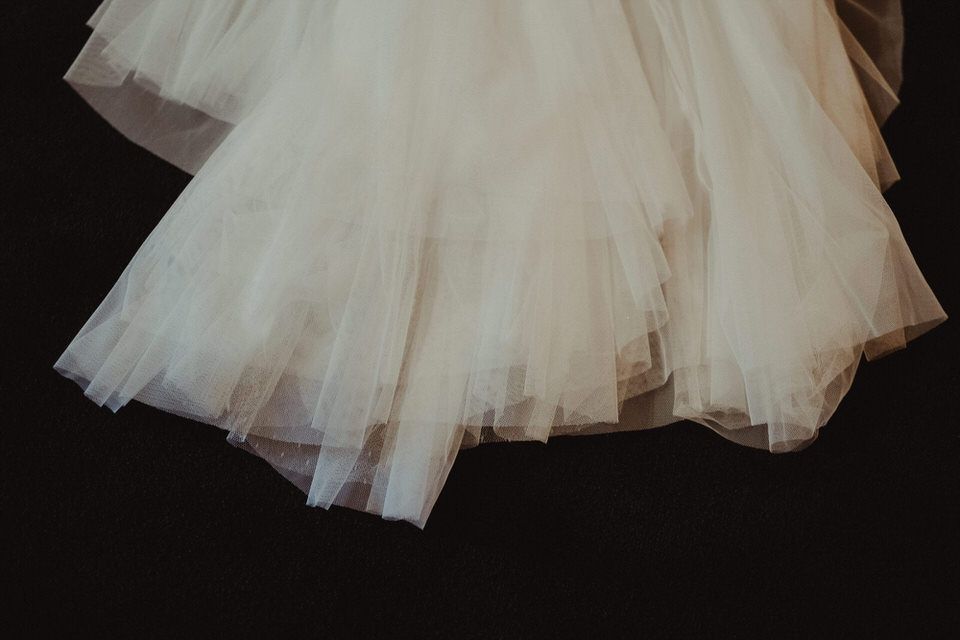 Detalhe em grande plano das camadas de tule branco de um vestido de noiva sobre um fundo preto.