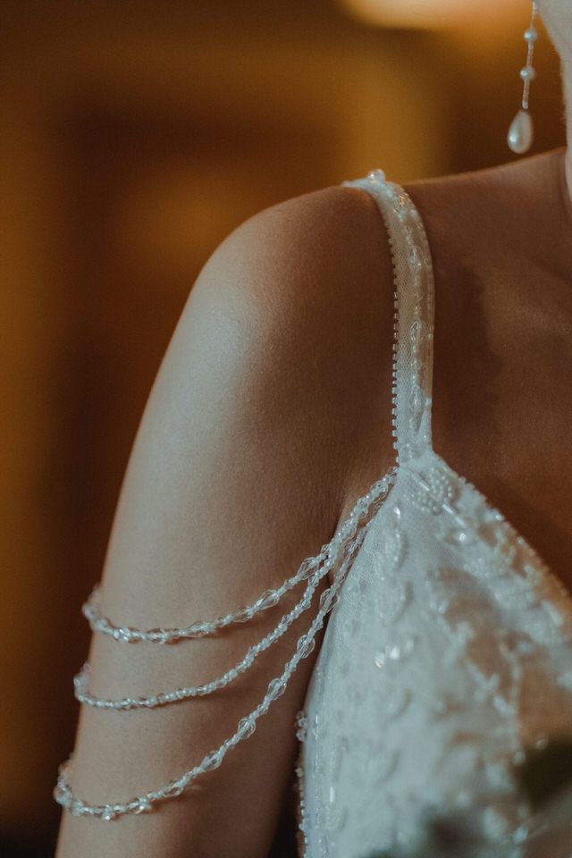 Pormenor em grande plano de um delicado bordado com missangas no ombro de um vestido de noiva branco.