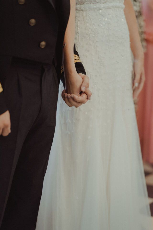 Um casal de mãos dadas, mostrando o contraste entre os trajes de cerimónia de casamento.
