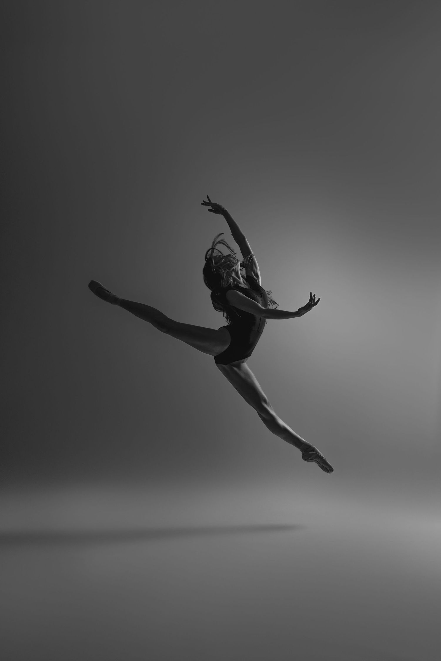 Black and white photo of dancer executing perfect split leap with graceful arm positioning.