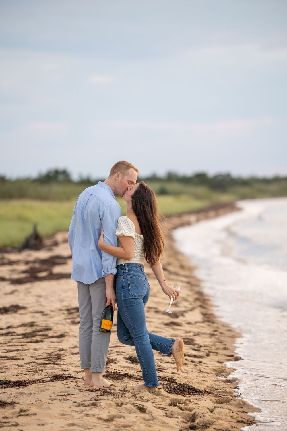 Romantic beach moment with barefoot couple holding drinks at shoreline.