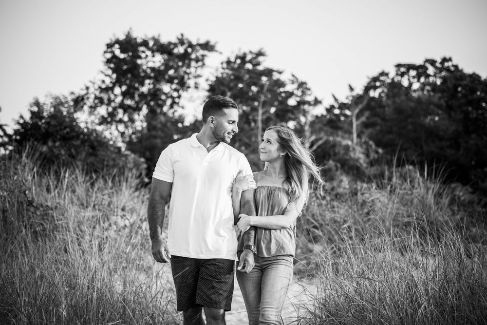 A casual black and white portrait of a couple walking through tall grass outdoors.