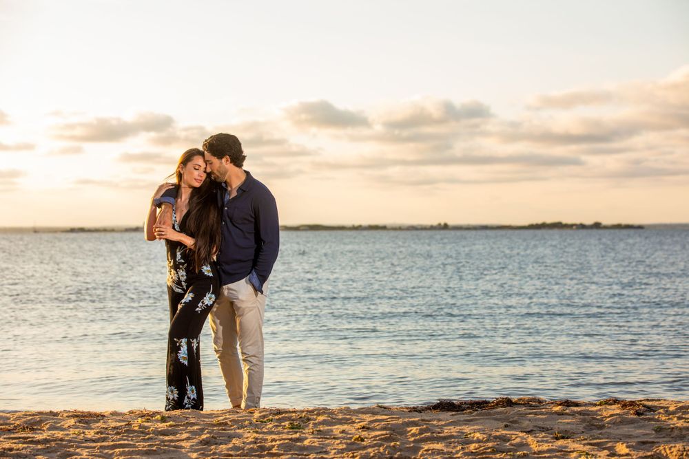 Couple sharing tender moment on beach at sunset with calm waters in background.