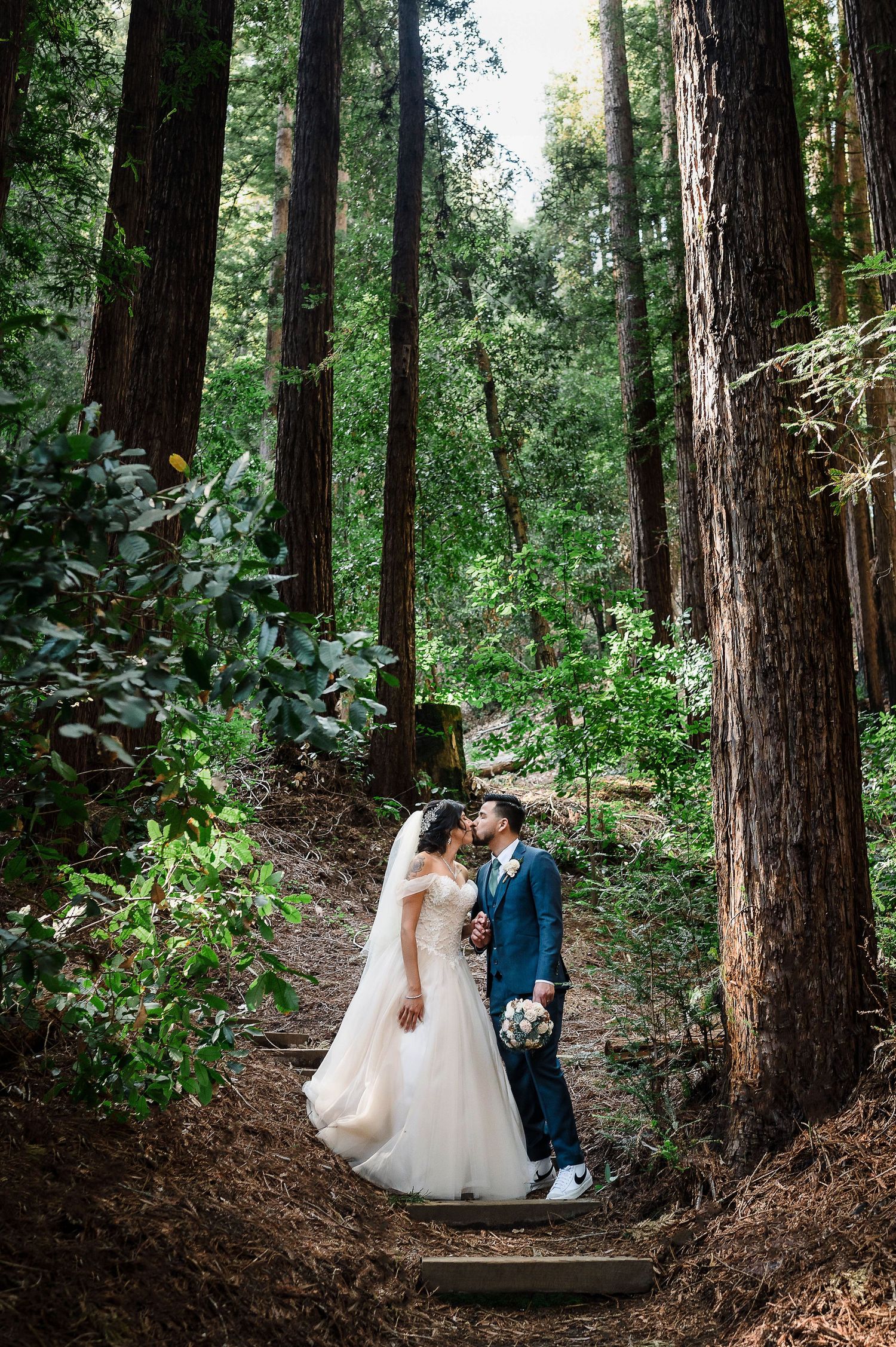 A couple shares an intimate moment on forest steps surrounded by majestic redwood trees.