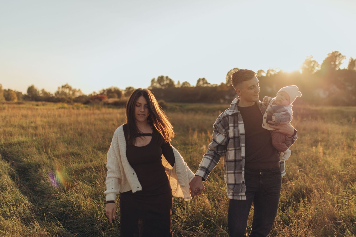 A family walks together through a golden field at sunset.