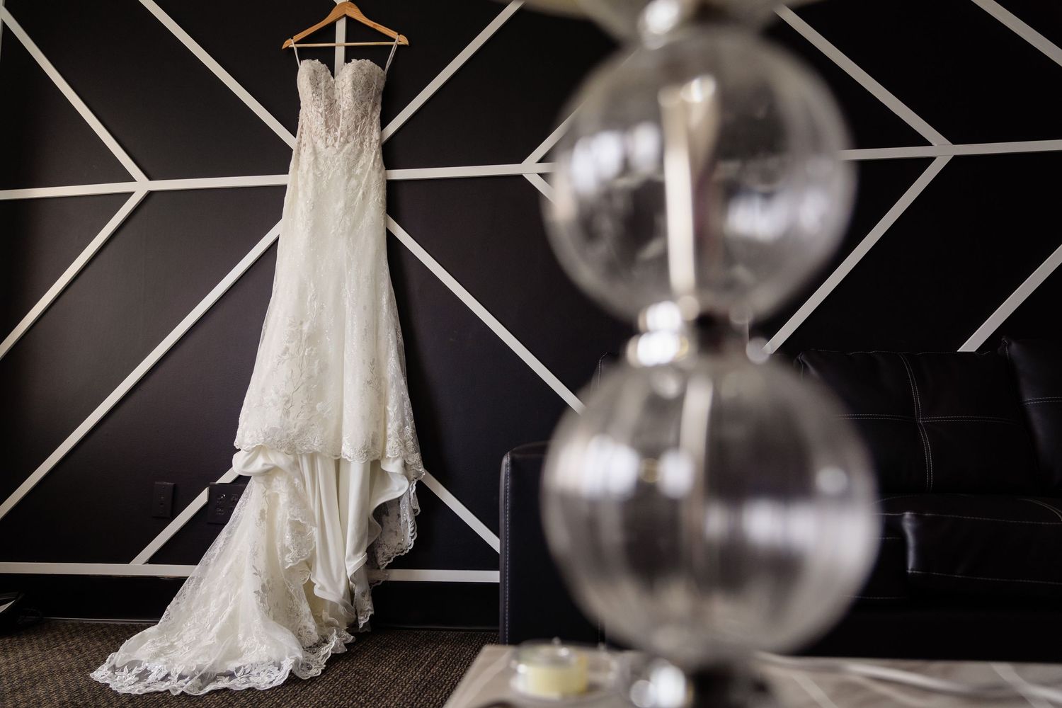 An elegant white wedding dress hangs against a geometric wall with modern light fixtures.