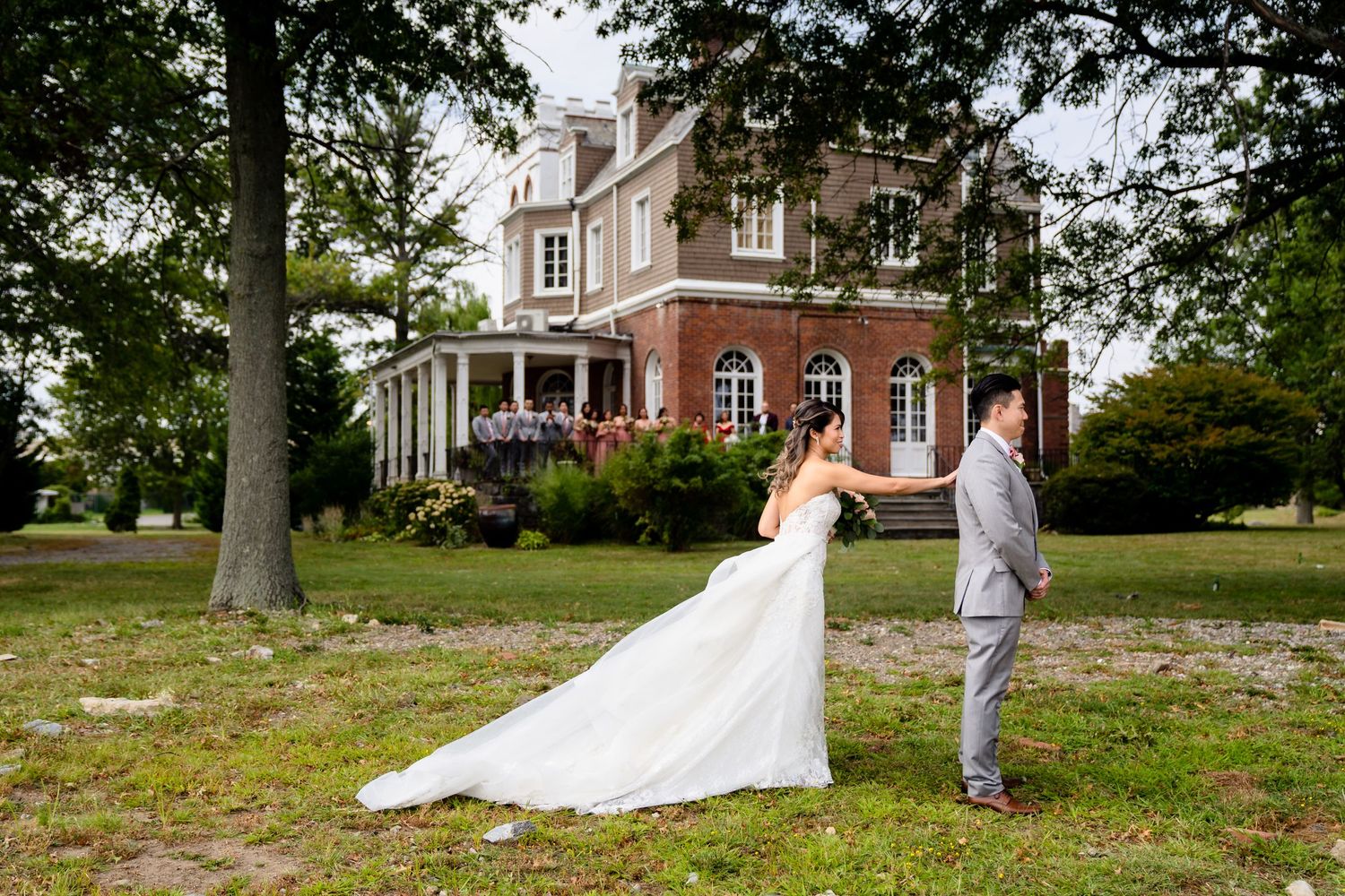 Newlyweds pose in front of grand brick mansion with sprawling grounds.