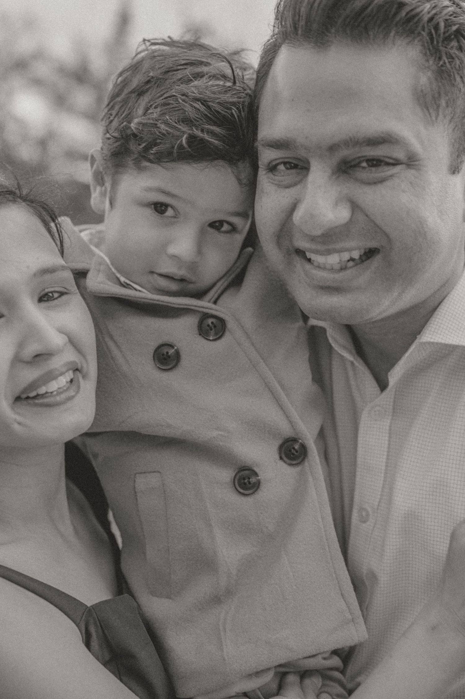 Black and white family portrait of three people embracing and smiling warmly.
