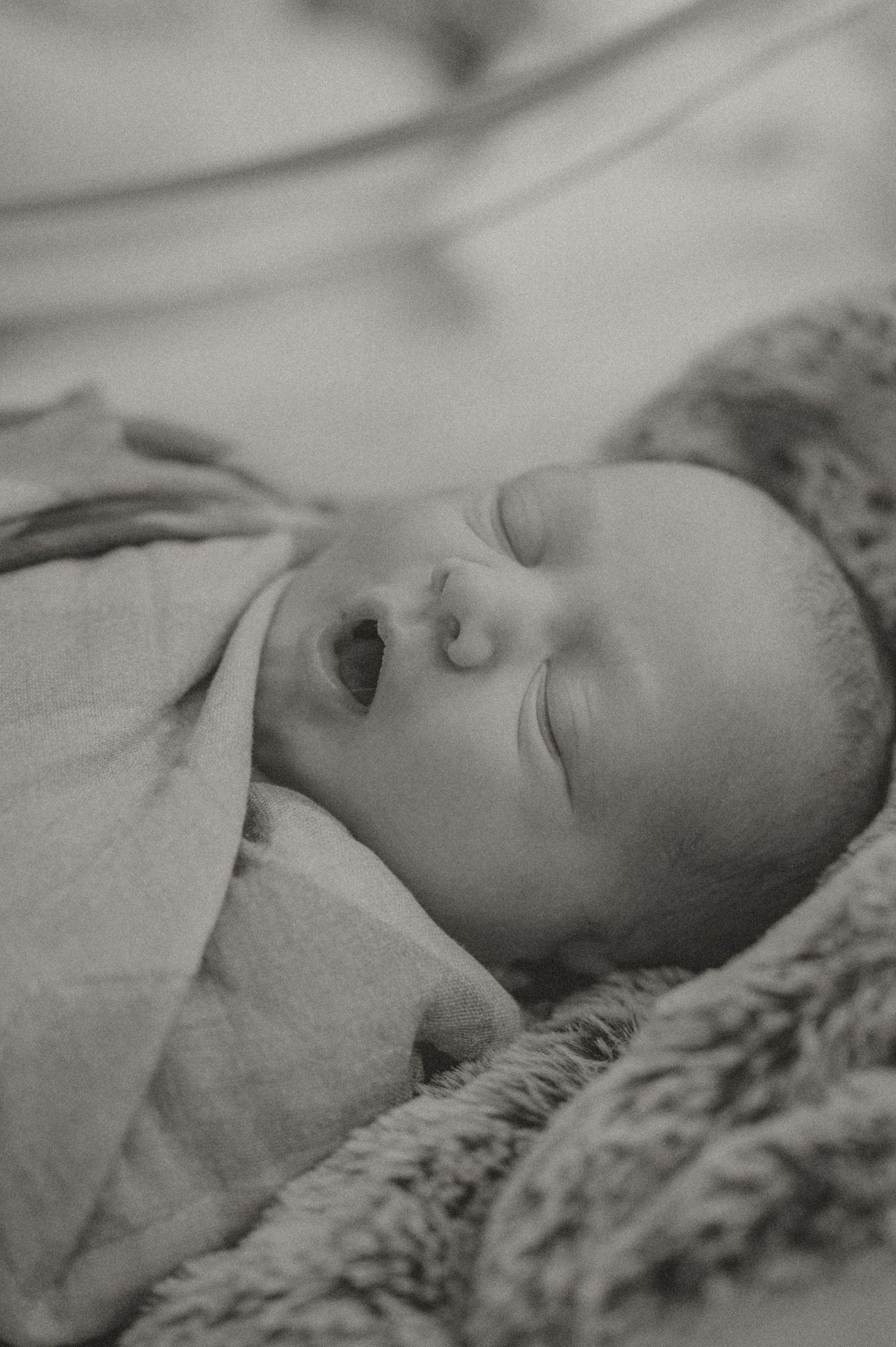 A black and white photograph of a young baby laying on a soft textured blanket.