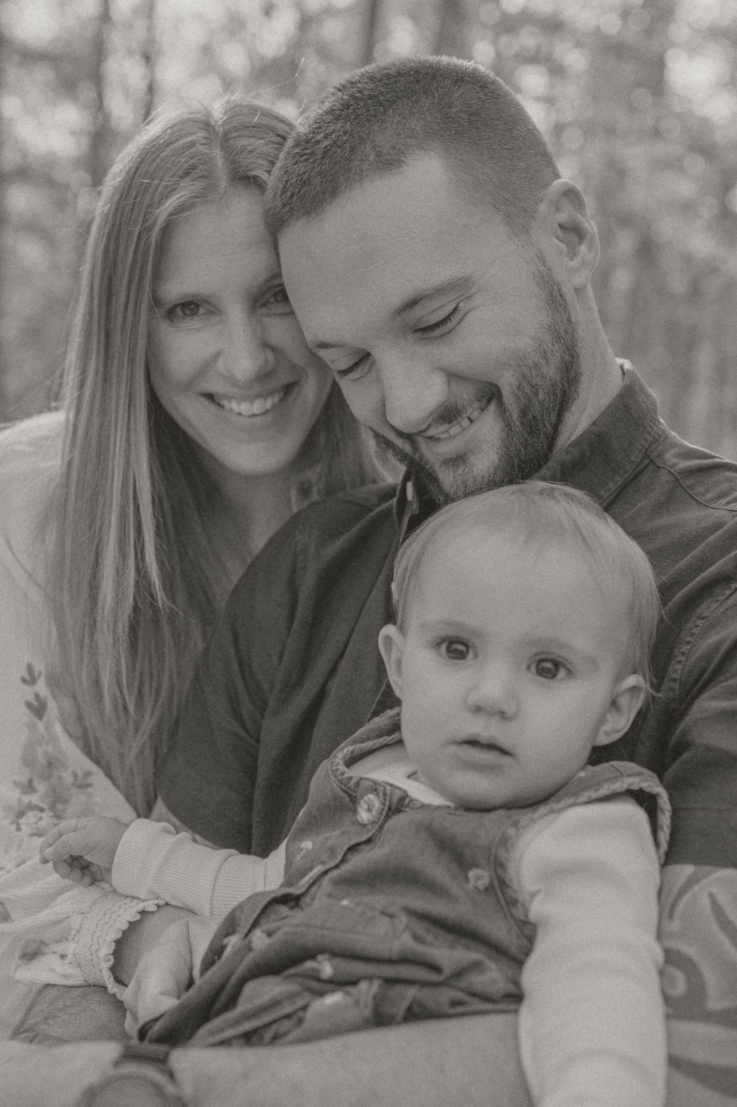 Black and white portrait of a young family with small child outdoors in a natural setting.