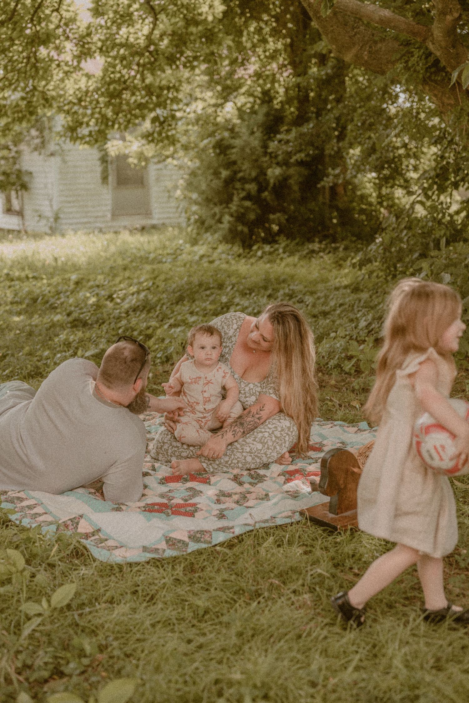 Family enjoying a outdoor picnic on a quilt, parents with baby and young daughter in lush garden.