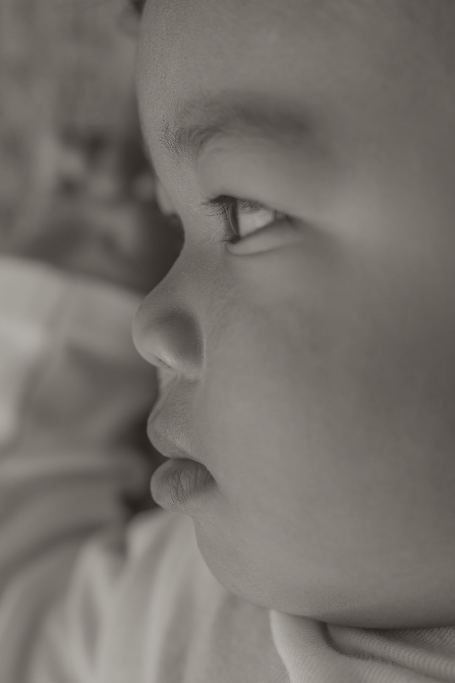 Close-up black and white portrait of a young baby gazing upward with soft, delicate facial features.