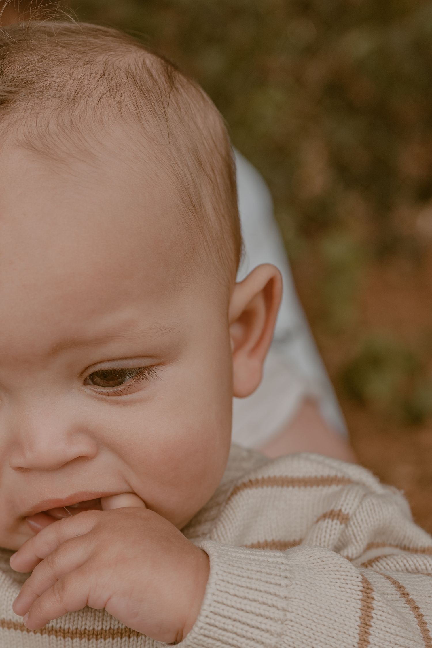 Close-up portrait of a curious baby in a beige knit sweater with fingers near mouth.