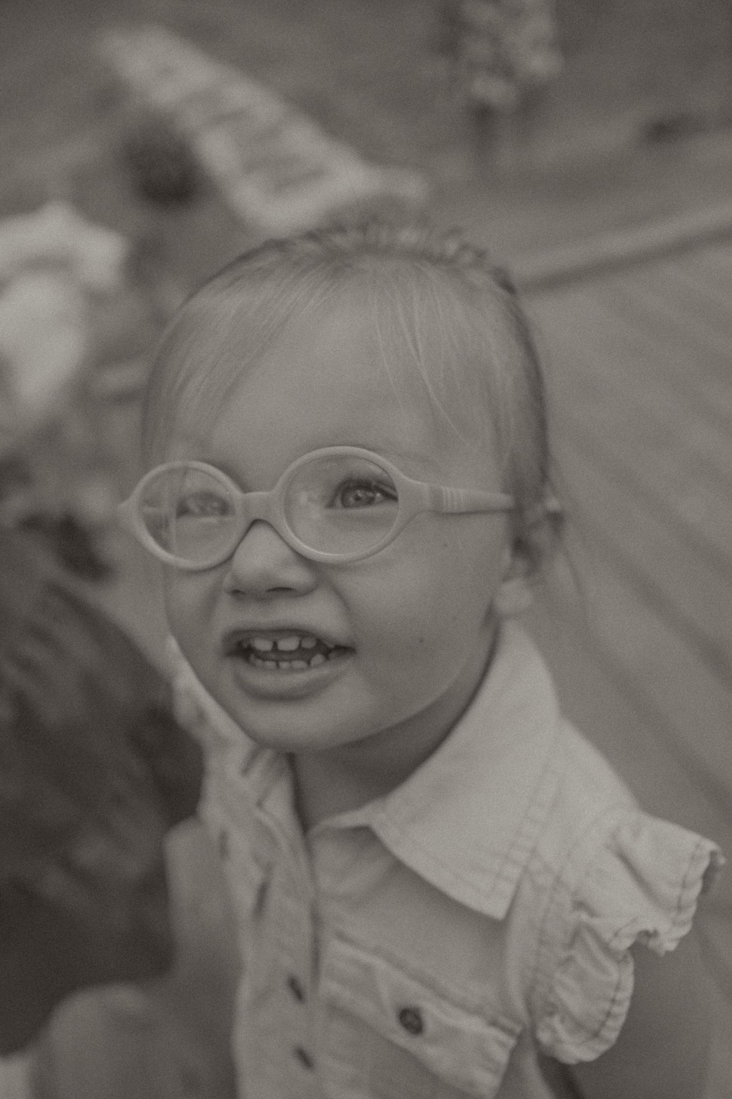 Black and white photo of a smiling young girl wearing round glasses and a ruffled collar dress.