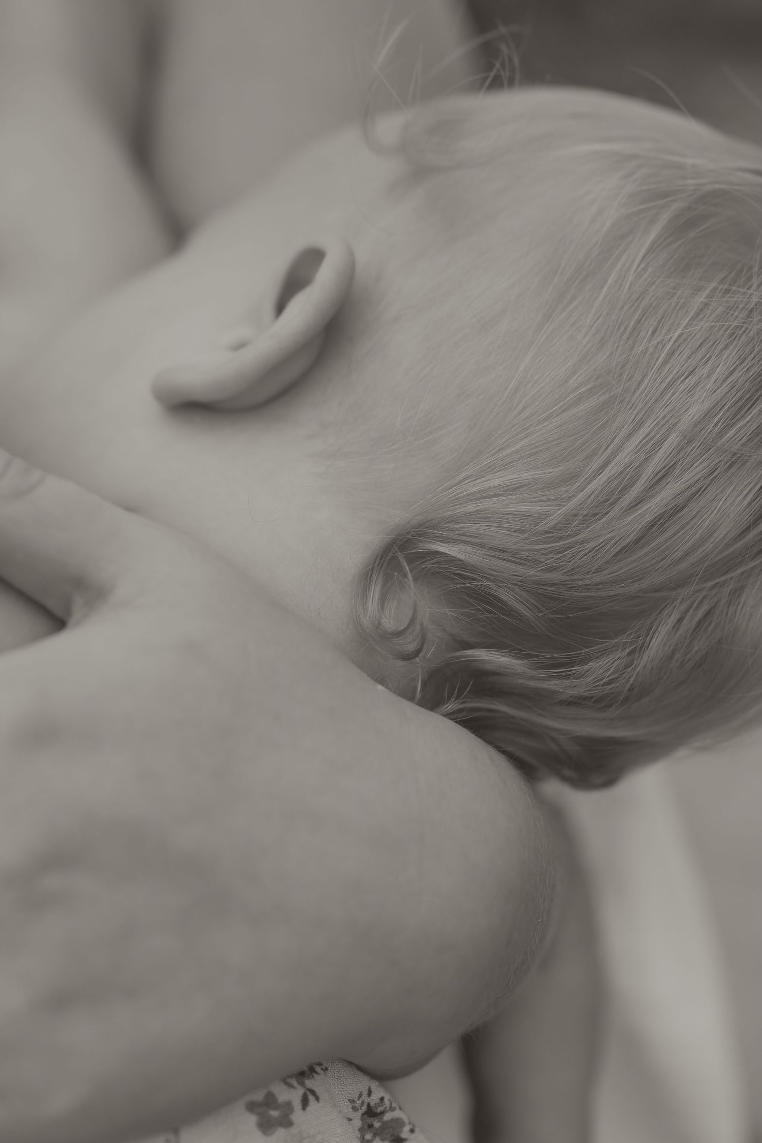 Black and white photo of a mother tenderly cradling her newborn baby's head while breastfeeding.