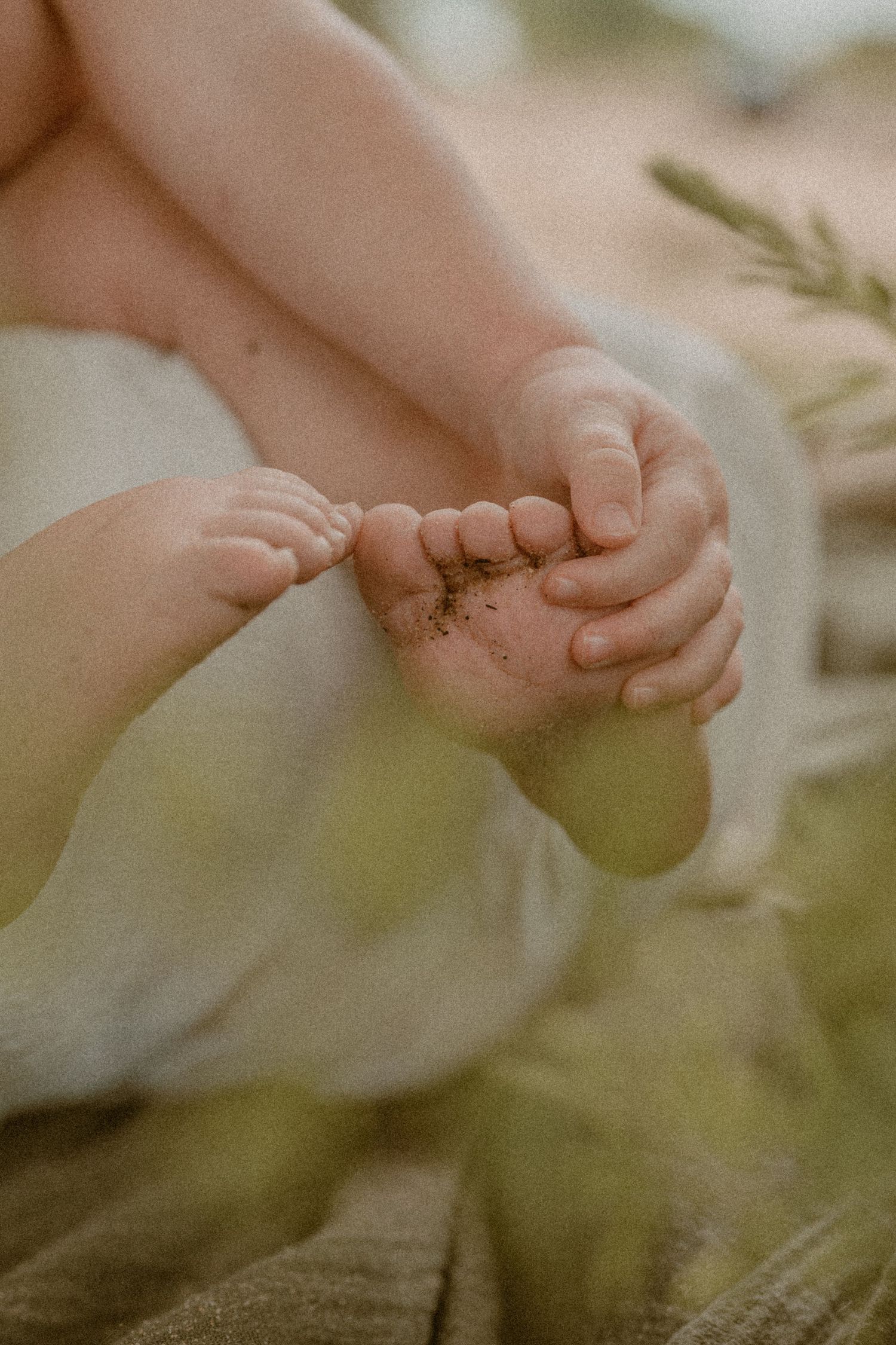Close-up of a baby's tiny feet held gently by small hands, with a soft green background.