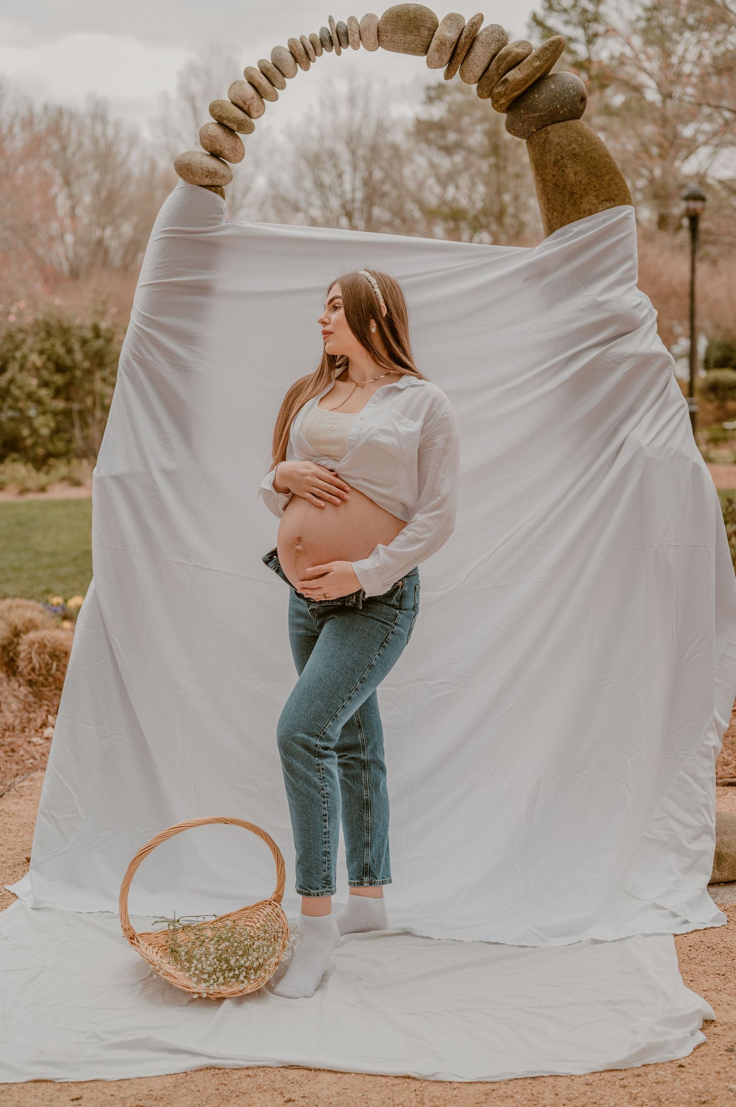Maternity photo against white backdrop with rustic arch and basket outdoors during autumn.