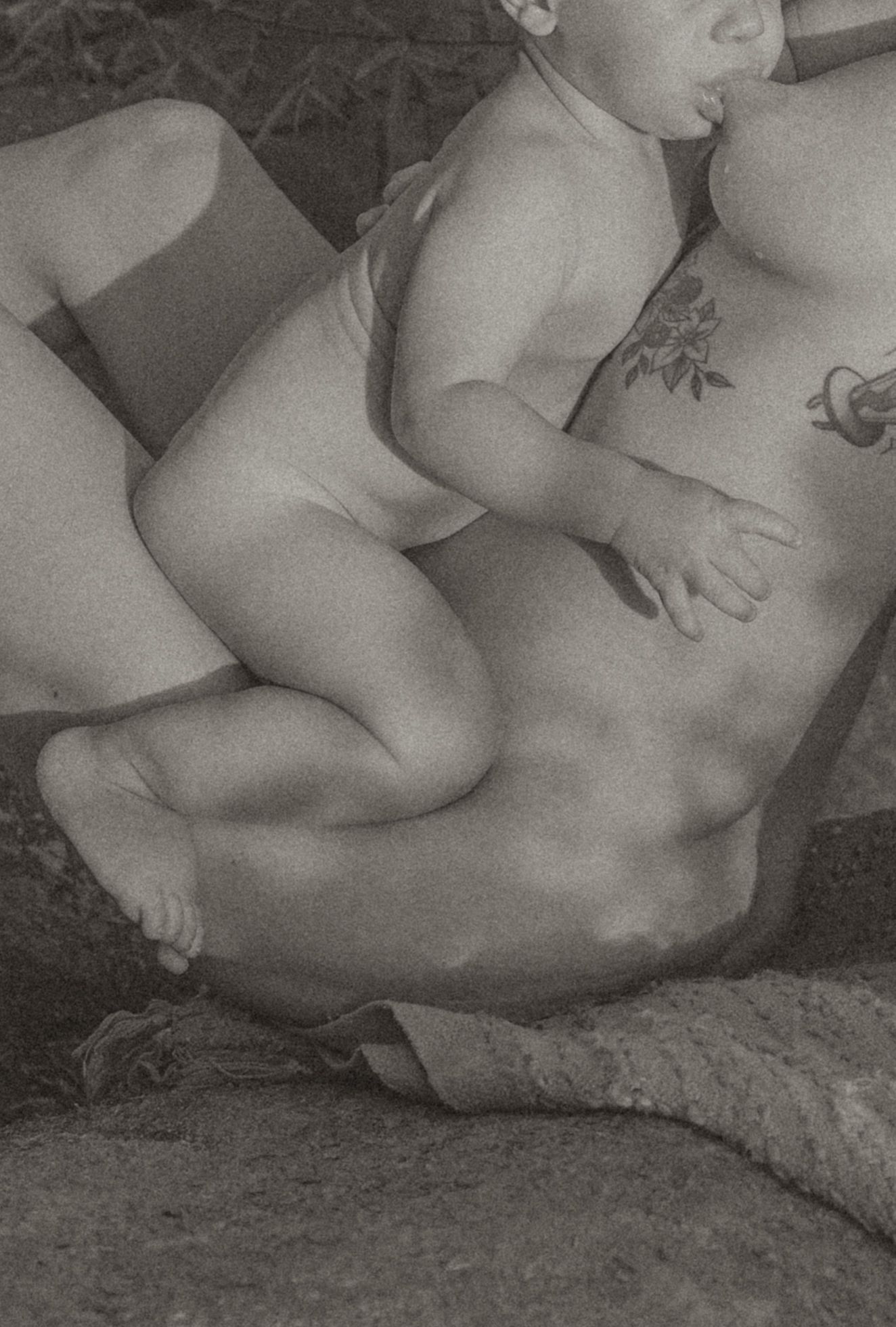 Black and white photo of a parent holding a baby outdoors, with a floral tattoo visible on the adult's arm.