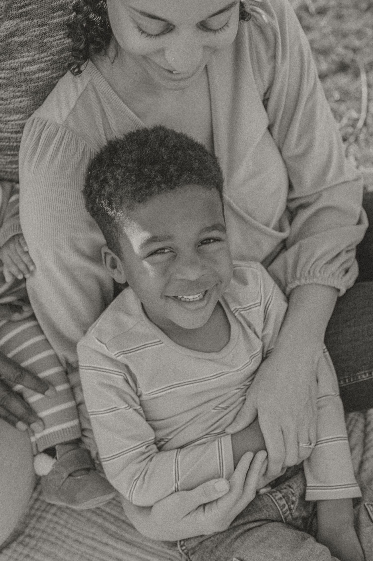Black and white photo showing a tender moment between two people embracing while sitting on a plaid blanket outdoors.