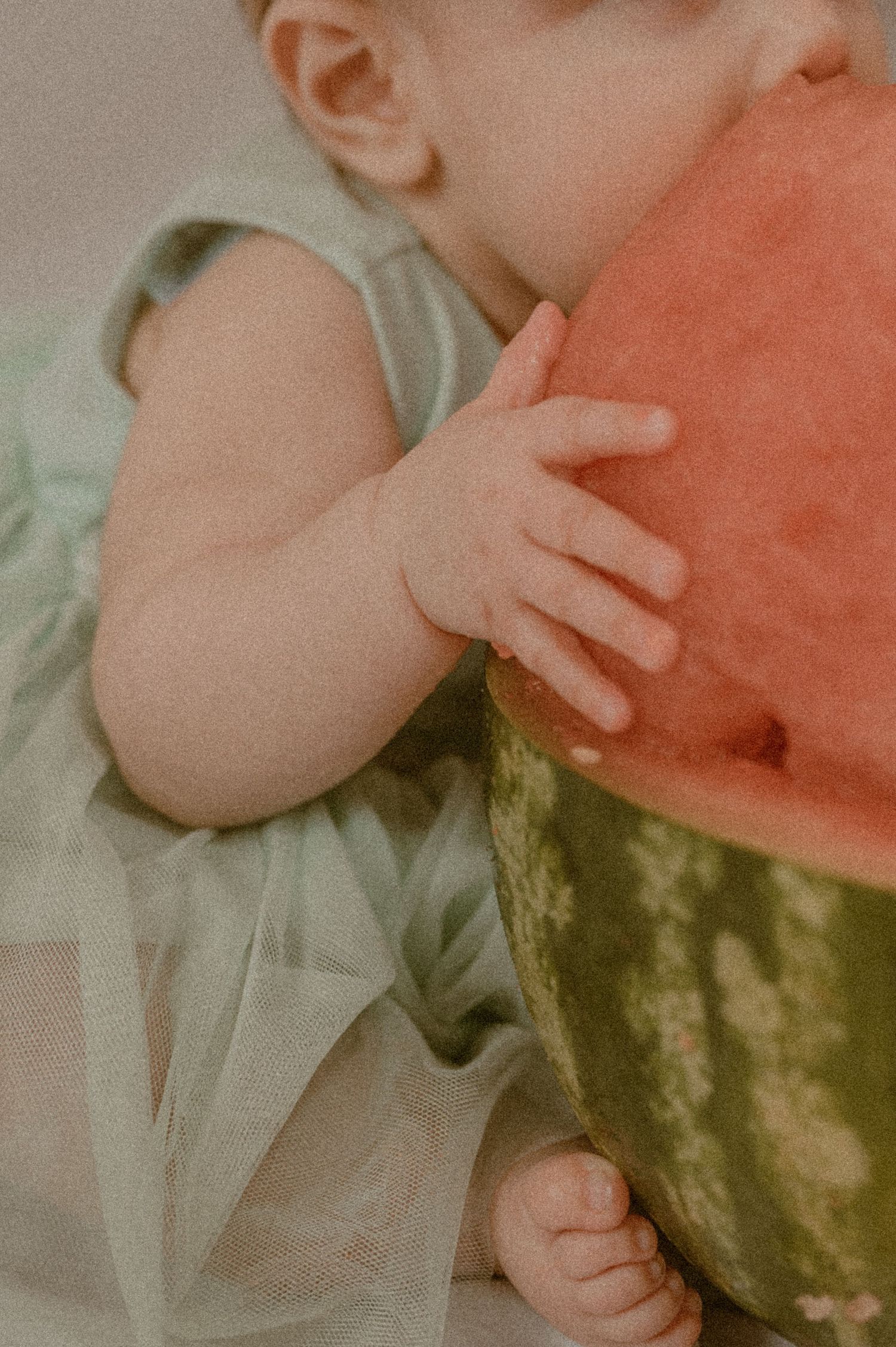 Close-up of small baby hands touching a large watermelon in soft vintage lighting.
