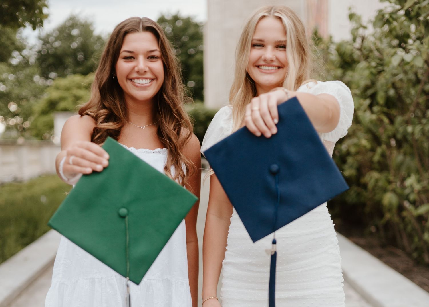 Two graduates displaying colorful graduation caps in outdoor setting.