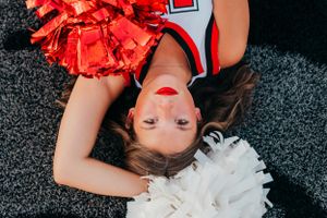 Cheerleader posing with red and white pom poms during photo shoot on field.