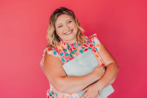 Person in floral print dress hugging themselves against bright pink background.