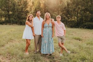 Family group posing together in sunlit meadow wearing coordinated outfits.