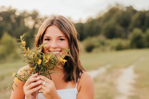 A senior holding fresh wildflowers outdoors in natural summer setting.